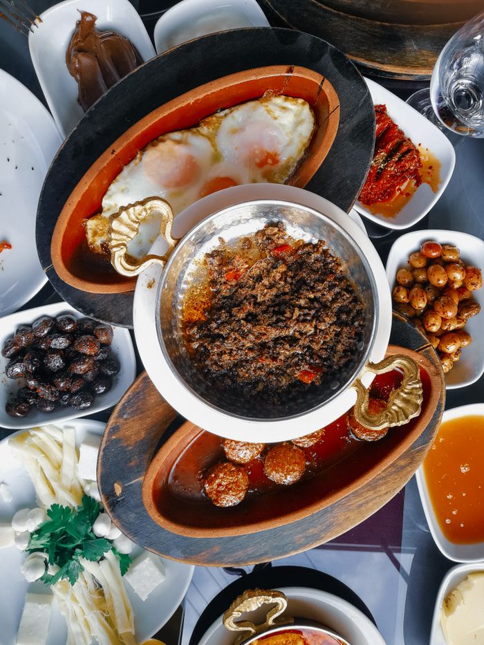 Services A rich assortment of breakfast foods, including eggs, olives, and dips, beautifully arranged on a table.