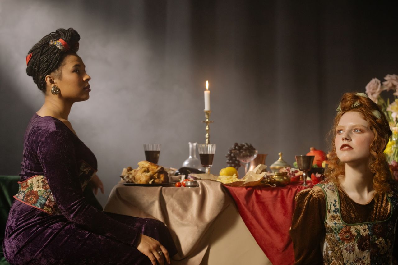 Elegant dining scene with two women in vintage fashion attire surrounded by a lavish feast.